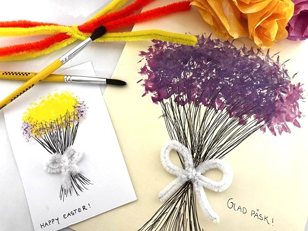 Påskpyssel med målade blombuketter i lila och gult, skapade med penslar och piprensare som dekoration, tillsammans med texten ’Glad Påsk’ och ’Happy Easter’.