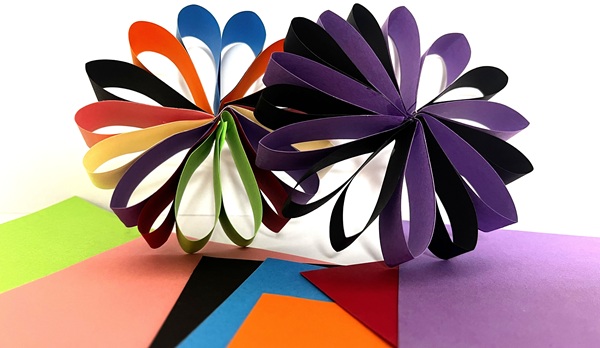 Färgglada pappersblommor gjorda av vikta papper i olika nyanser, omgivna av ark i starka färger.