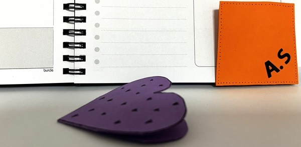 Handgjort pappershjärta och färgad etikett placerade framför en öppen spiralbunden kalender.