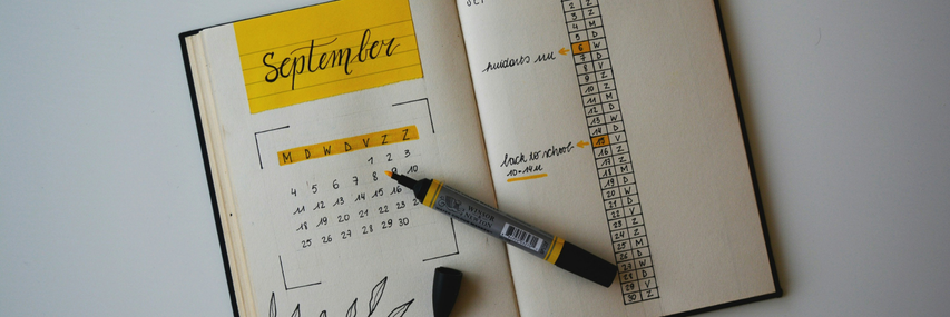 Öppen anteckningsbok med septemberkalender, markerade datum och pennor