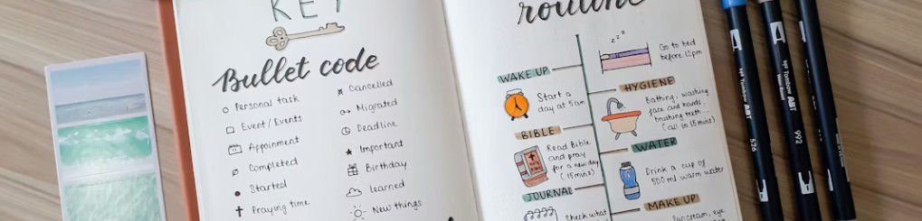 Öppen bullet journal med en nyckel för symboler och en illustrerad morgonrutin, bredvid färgpennor och ett fotoark.