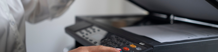 Hand som trycker på knappar på en kopiator med locket öppet.
