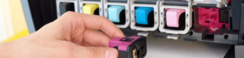 Närbild på en person som installerar en magentafärgad bläckpatron i en färgskrivare. Skrivaren har fyra fack för bläckpatroner: svart, cyan, gul och magenta. Personens hand håller magentapatronen nära dess plats.