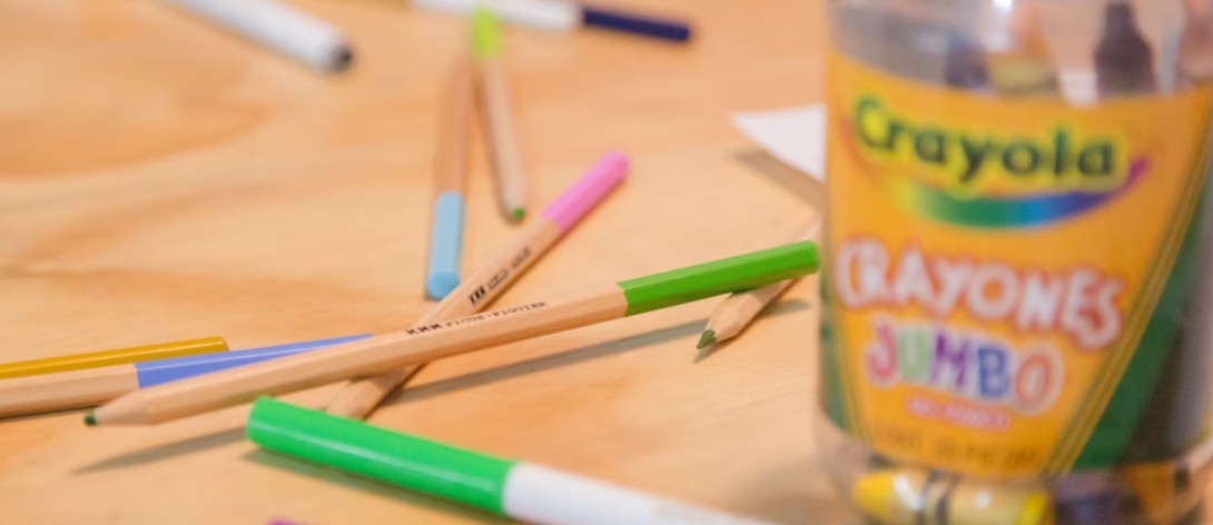 Färgpennor i olika färger utspridda på en träyta, med en delvis synlig Crayola Jumbo förpackning till höger