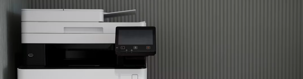 Multifunktionsskrivare med pekskärm sedd från sidan mot en räfflad vägg.