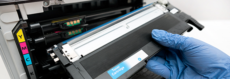 Hand med skyddshandske sätter in en tonerkassett i en laserskrivare.