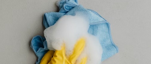 Gul rengöringshandske med skum ovanpå blå mikrofiberduk vid städning.